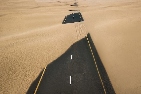 black paved road through desert with sand drifted over it